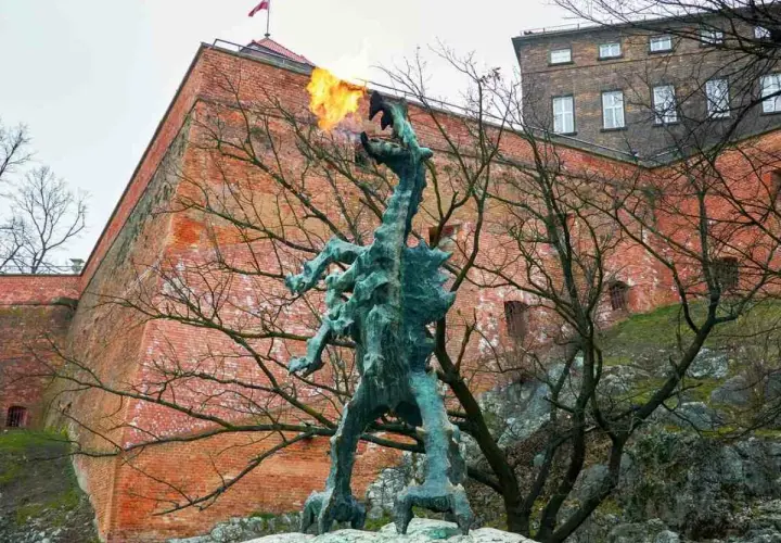 Smok Wawelski ziejący ogniem, pomnik nawiązujący do legendy, na tle ceglanych murów Wawelu.
