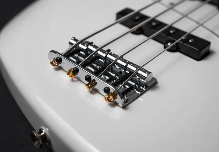 Błyszczące, chromowane struny do gitary basowej 4 strunowej na białym korpusie instrumentu.