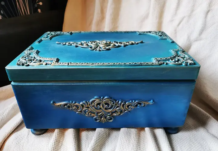 Elegancka, turkusowa skrzynia na skarby z ozdobnymi, złotymi ornamentami. Idealna do przechowywania cennych drobiazgów.