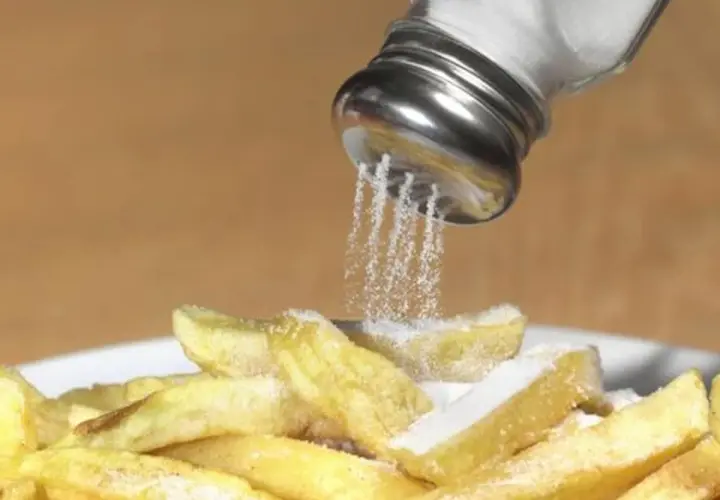 Salzstreuer rieselt Salz auf Pommes. Zu viel Salz essen kann zu Problemen führen.
