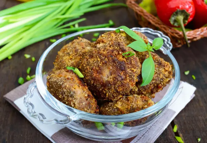 Chrupiące mielone z pieczarkami w szklanej misie, ozdobione listkami bazylii i szczypiorkiem. Obok pęczek zielonej cebulki i czerwone papryczki.