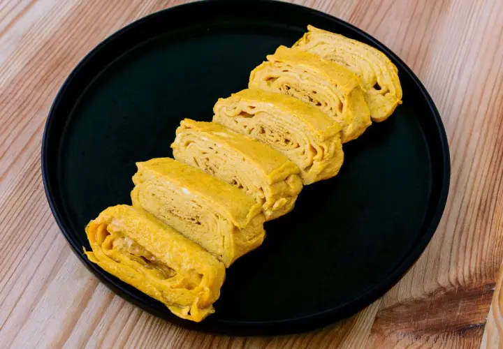 Tranches d'oeuf tamago, un délice japonais, disposées sur une assiette noire.