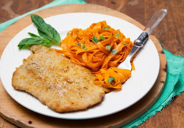 Escalope de veau panée, servie avec des tagliatelles de carottes et des feuilles de basilic. Une recette simple et savoureuse.