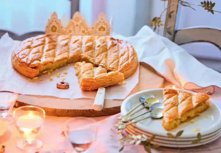 Une galette des rois dorée, prête à être partagée, avec une couronne posée à côté. Une part est déjà servie, invitant à la fête.