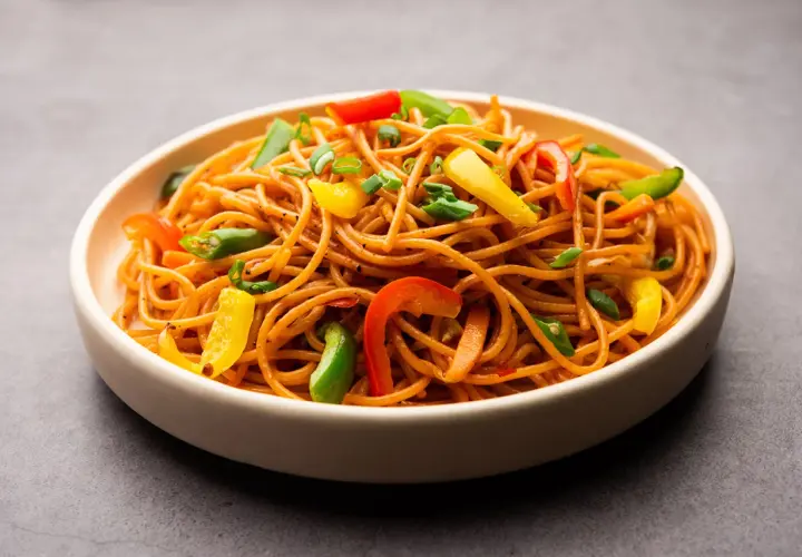 Un plato de espaguetis con verduras salteadas, con pimientos de colores y cebolleta.