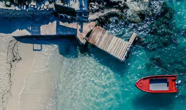 Traumhafter Urlaub im August: Sandstrand, Holzsteg und ein rotes Boot im türkisfarbenen Meer.