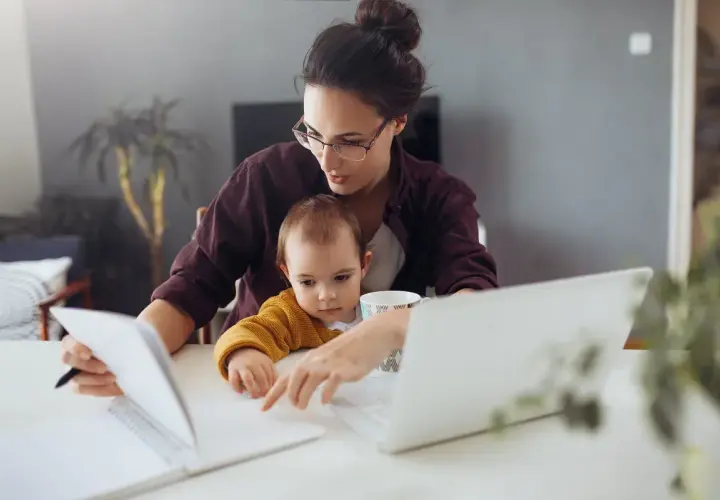 Mama z dzieckiem przy biurku, pracująca zdalnie. Kosiniakowe dla kogo? Dla wszystkich rodziców łączących pracę z opieką nad dzieckiem.