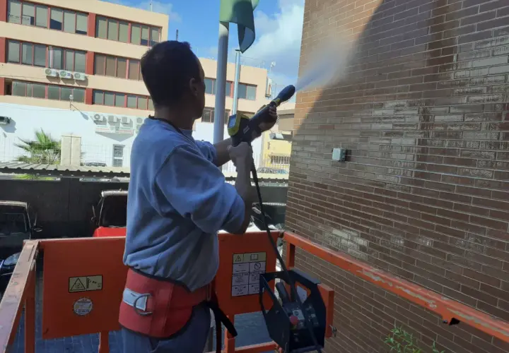 Hombre en plataforma elevadora realiza limpieza de fachadas con agua a presión, dejando la pared de ladrillo brillante y reluciente.