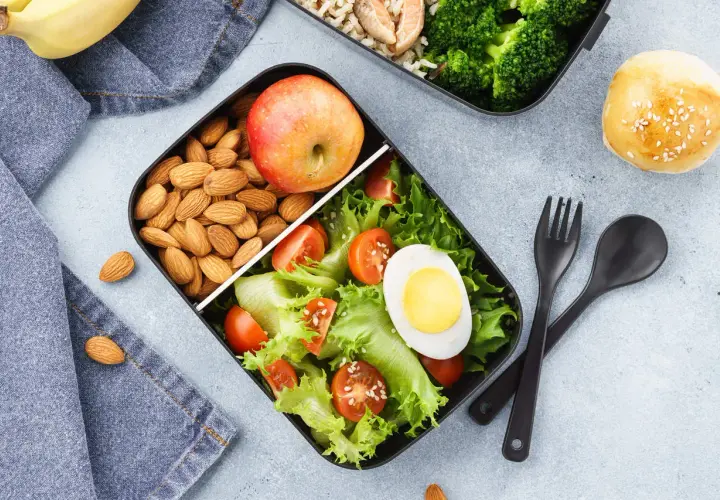 Pudełko na lunch z sałatką, jajkiem, pomidorkami, migdałami i jabłkiem.