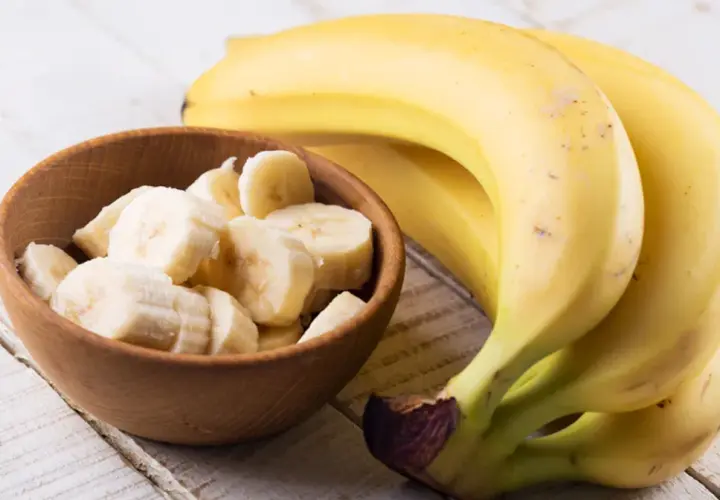Dojrzały banan kcal w miseczce i pęczek bananów na drewnianym stole.