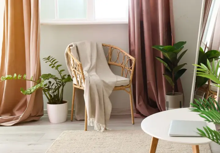 A cozy reading nook with a wicker chair draped in a blanket, flanked by pooled curtains in soft peach and dusty rose hues.