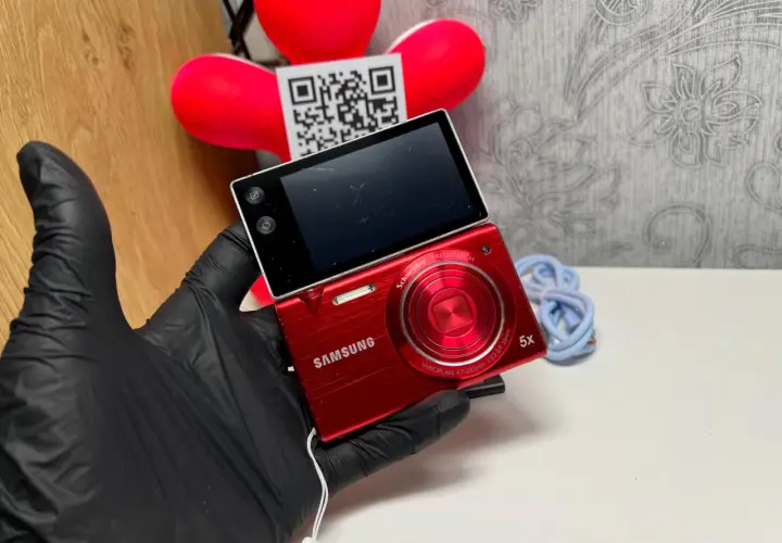 Czerwony aparat Samsung MV800 z obracanym ekranem, trzymany w czarnej rękawiczce.