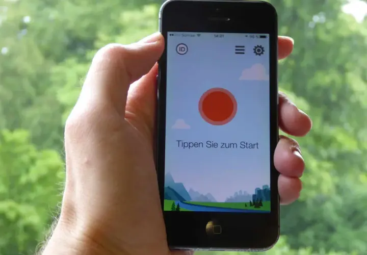 Ein Smartphone wird gehalten, um Vogelstimmen vorspielen zu lassen. Die App zeigt eine Landschaft und den Text "Tippen Sie zum Start".