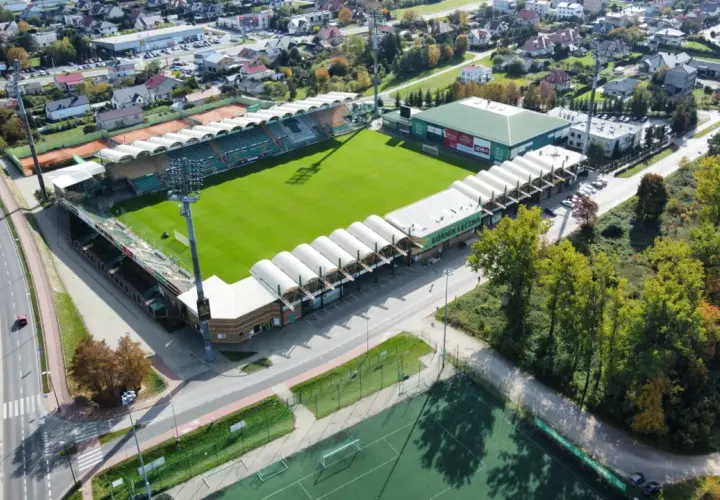 Widok z lotu ptaka na stadion Górnik Łęczna z zieloną murawą, trybunami i otaczającymi go budynkami.