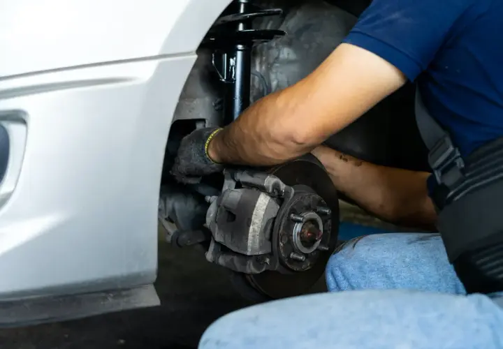 Mecánico trabajando en el sistema de frenos y amortiguadores de un coche. Merece la pena cambiar amortiguadores para una conducción segura.