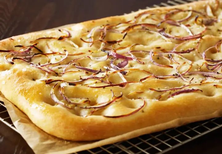 Focaccia dorada con finas rodajas de cebolla balsámica y sal gruesa, recién salida del horno.