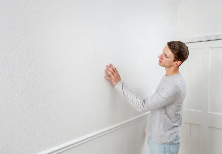Man undersöker en vit vägg, kanske för att ta bort tapet.