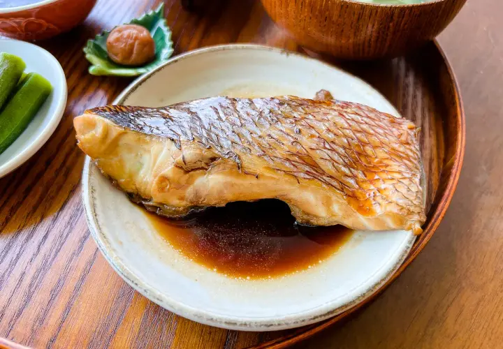 A perfectly cooked piece of karei no nitsuke, its skin crisped and glazed, rests in a savory sauce. Served with pickled plum and okra.