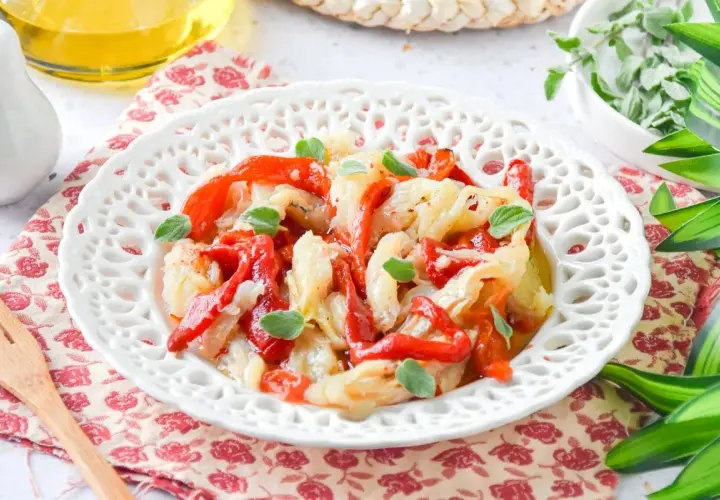 Deliciosa ensalada de bacalao con pimientos rojos asados y hierbas frescas, servida en un plato blanco decorado.