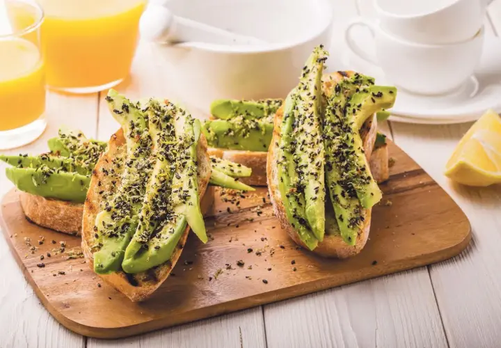 Tostadas con aguacate y semillas negras, perfectas para desayunos veganos. Acompañadas de zumo de naranja y limón.