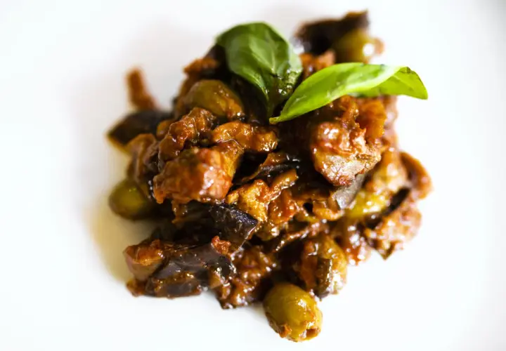 Un saporito piatto di caponata di pesce spada, con melanzane, olive e basilico fresco, pronto per essere gustato.