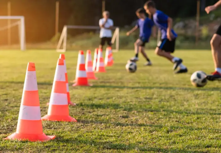 Trening piłkarski z użyciem pachołków, pokazujący jak uczyć futbolu. Dzieci ćwiczą drybling na boisku.