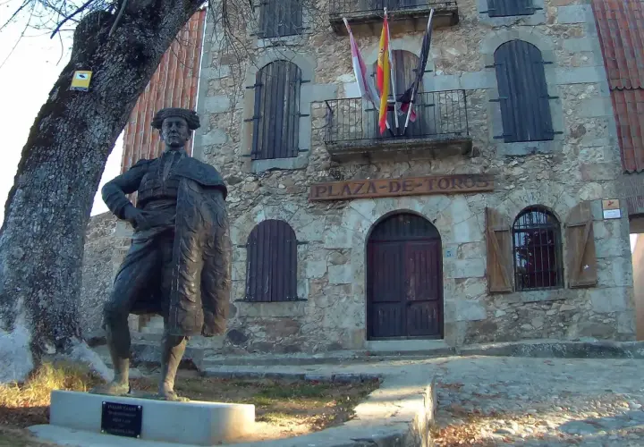 Estatua de un torero frente a la plaza de toros la ancianita. El edificio de piedra tiene un letrero y banderas españolas.