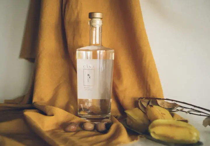 Butelka Cachaça Cãna, brazylijskiego alkoholu z trzciny cukrowej, otoczona owocami i suchymi liśćmi. Cachaca co to? To brazylijski skarb!