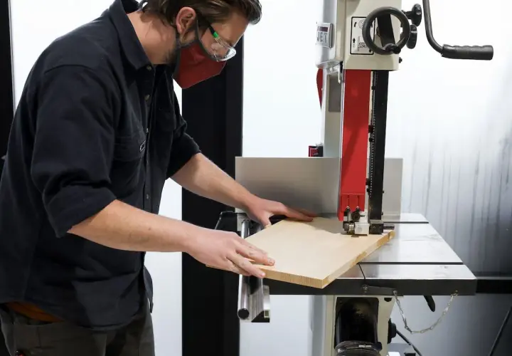 Un artisan utilise une scie à ruban, un des outils pour couper le bois, pour façonner une planche.