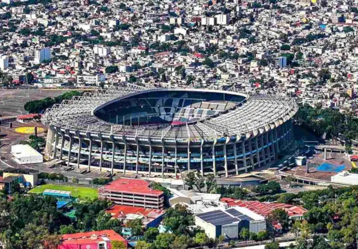 Widok z lotu ptaka na monumentalny stadion Azteca otoczony gęstą zabudową miejską.