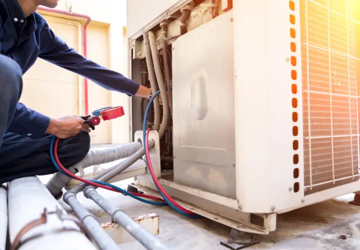 Técnico realiza soldadura con nitrógeno en unidad de aire acondicionado exterior, conectando manómetros a tuberías.