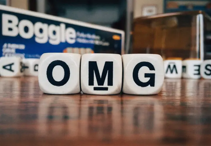 Dadi con lettere formano l'acronimo in inglese "OMG". Sullo sfondo, la scatola del gioco Boggle.