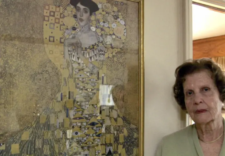 Eine ältere Frau steht neben Gustav Klimts "Adele Bloch-Bauer I", einem goldenen Porträt mit geometrischen Mustern.
