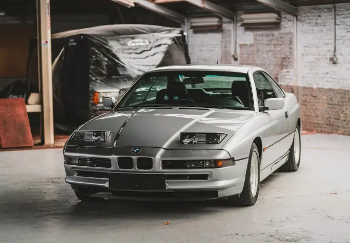 Un elegante BMW E31 plateado, un clásico deportivo, descansa en un garaje con paredes de ladrillo.
