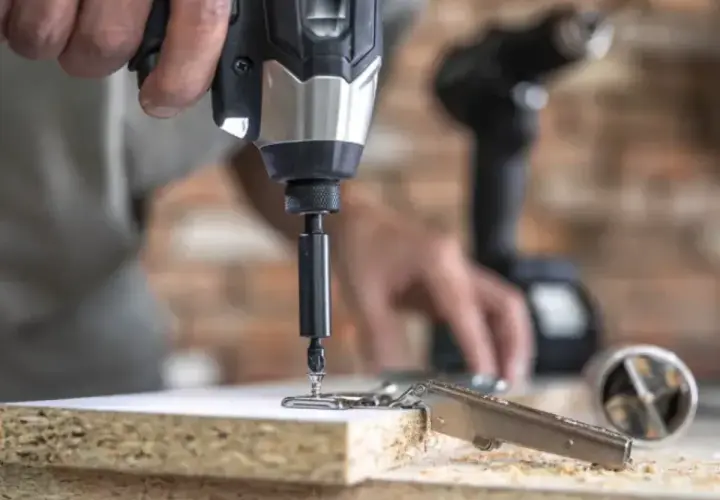 Instrucciones sobre como poner una broca en un taladro. Un hombre usa un taladro para fijar una bisagra a un tablero de madera.