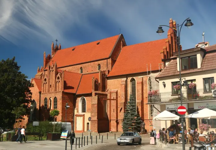 Starogard Gdański atrakcje: ceglana bazylika z czerwonym dachem i gotyckimi detalami, plac z kawiarnią i ludźmi.