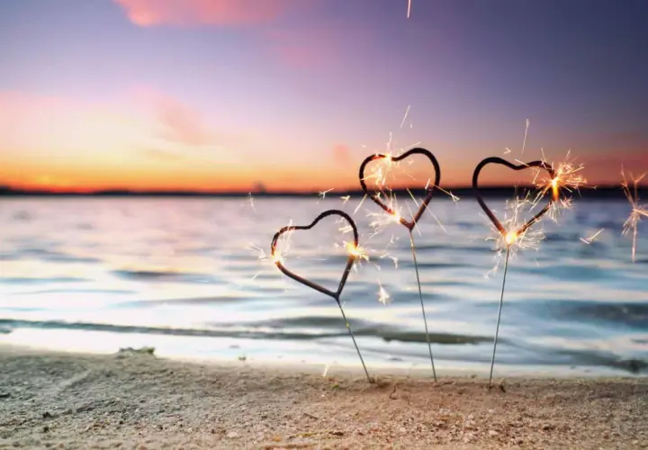 Drei Herz-Wunderkerzen funkeln am Strand. Ein romantischer Silvester am Meer mit einem farbenprächtigen Himmel.
