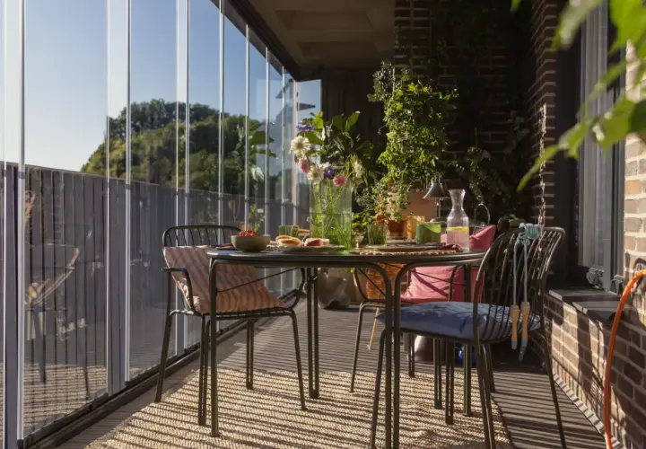 Jak zrobić balkon w bloku? Przytulny, przeszklony balkon ze stolikiem, krzesłami i mnóstwem zieleni. Idealne miejsce na poranną kawę.