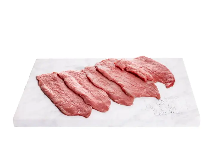 Fettine di vitello pronte per gustose ricette. Carne fresca su tagliere di marmo con sale grosso.