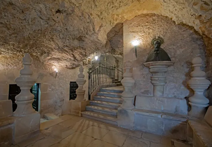 Busto de San Saturio en Soria, junto a escaleras de piedra y rejas, en un entorno rocoso.