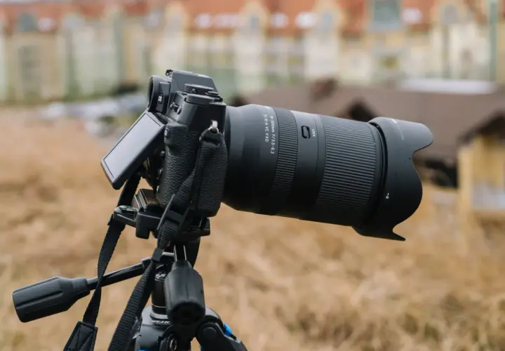 Aparat fotograficzny z obiektywem 18-300mm na statywie, z rozmytym budynkiem w tle.