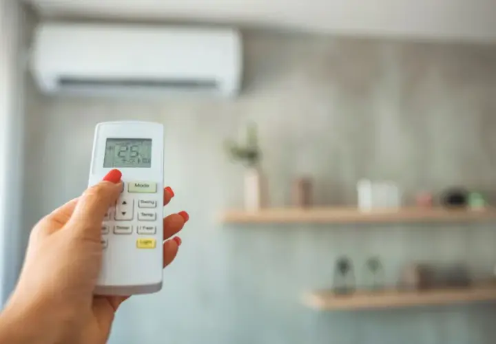 Mano con mando a distancia de aire acondicionado, ajustando la temperatura. Ideal para calcular potencia aire acondicionado y optimizar el confort.