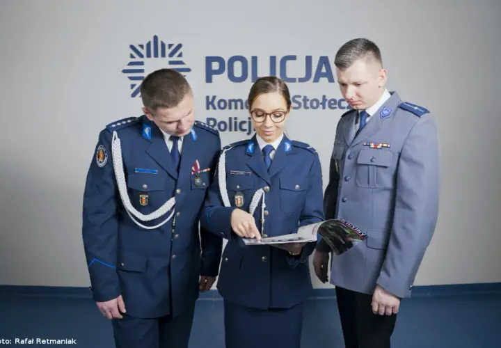 Policjanci w mundurach omawiają materiały. Pokazują, jak nosić furażerkę policja.