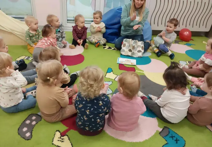 Nauczycielka pokazuje dzieciom w żłobku obrazki, inspirując angielski w żłobku pomysły. Dzieci siedzą na kolorowym dywanie.
