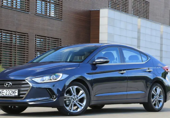 Ciemnoniebieski Hyundai Elantra 2023 zaparkowany przed nowoczesnym budynkiem z drewnianą fasadą.