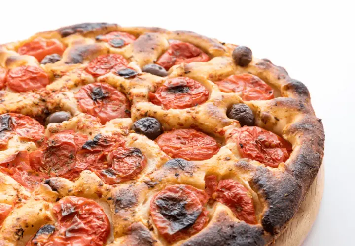 Focaccia barese dorata e fragrante, con pomodorini succosi e olive nere, pronta per essere gustata.