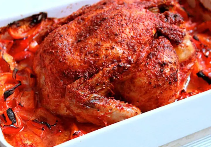 Helstekt tandoori kyckling med rostade tomater och paprika i en vit ugnsform. Kryddig och saftig.