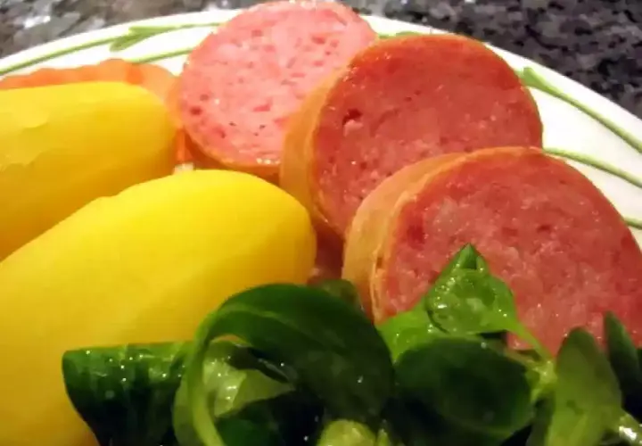 Tranches de saucisson savoureux accompagnées de pommes de terre jaunes et d'une salade verte fraîche.
