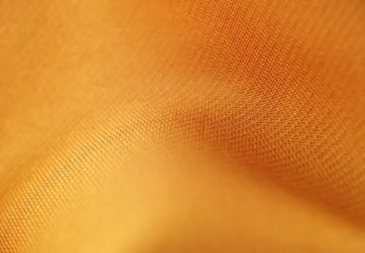 Texture d'un tissu orange vif, où chaque rayon fibre est visible, créant un motif subtil et doux.
