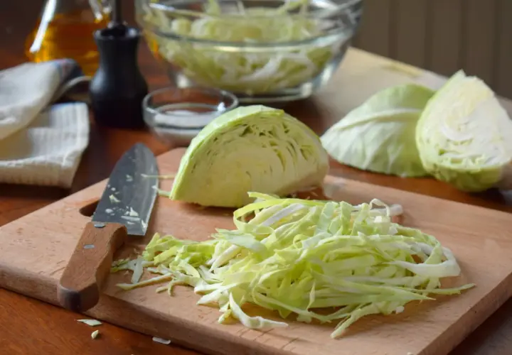 Frisch geschnittener Weißkohl liegt auf einem Holzbrett, bereit für ein Sauerkraut Rezept. Daneben ein Messer und Schüssel mit Kohl.
